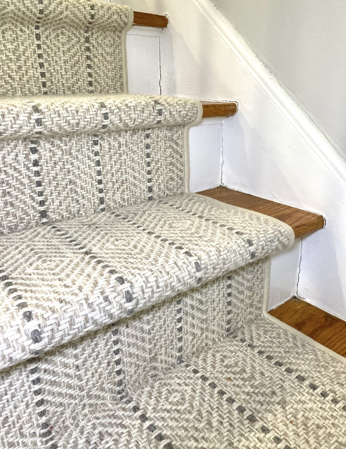 Close-up of a neutral geometric custom stair runner fitted around wood stair treads