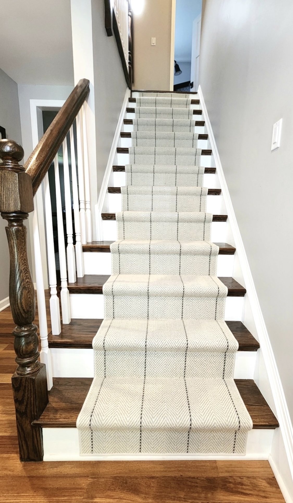 Modern neutral herringbone stair runner with dark vertical stripe details on wood stairs